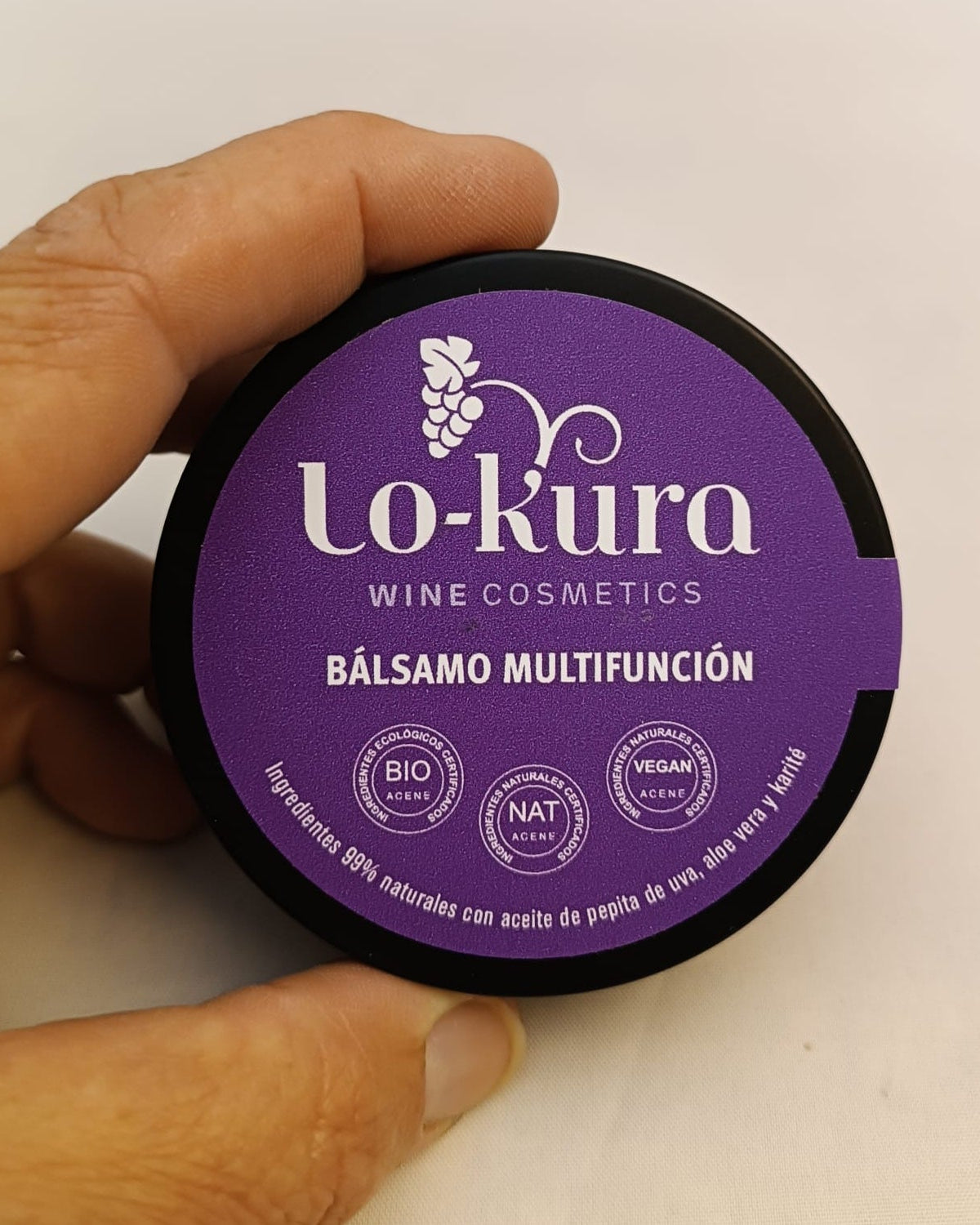 lata negra sujetada entre dos dedos con etiqueta morada donde se lee lo-kura wine cosmetics bálsamo multifunción