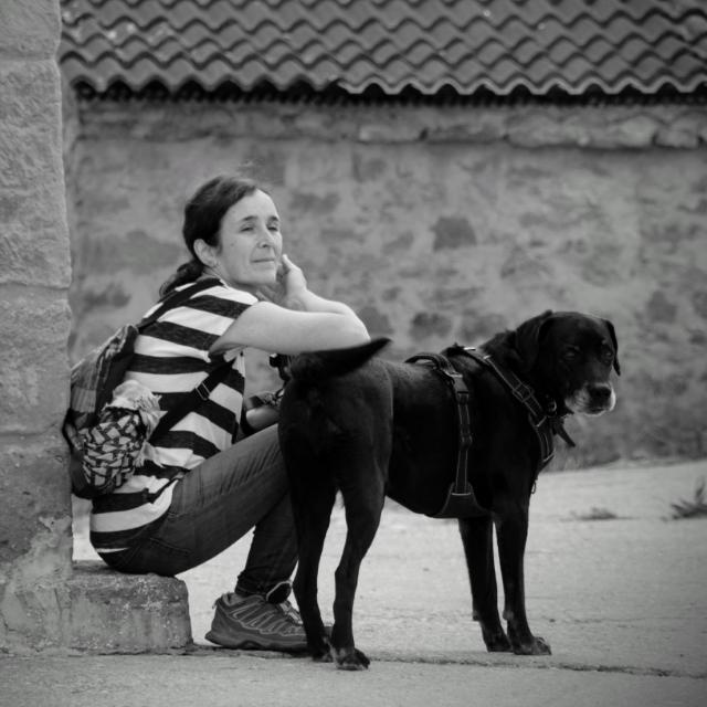 foto mujer sentada con camiseta a rayas negra y blanca apoyada en perro negrocon morro blanco que mira a cámara
