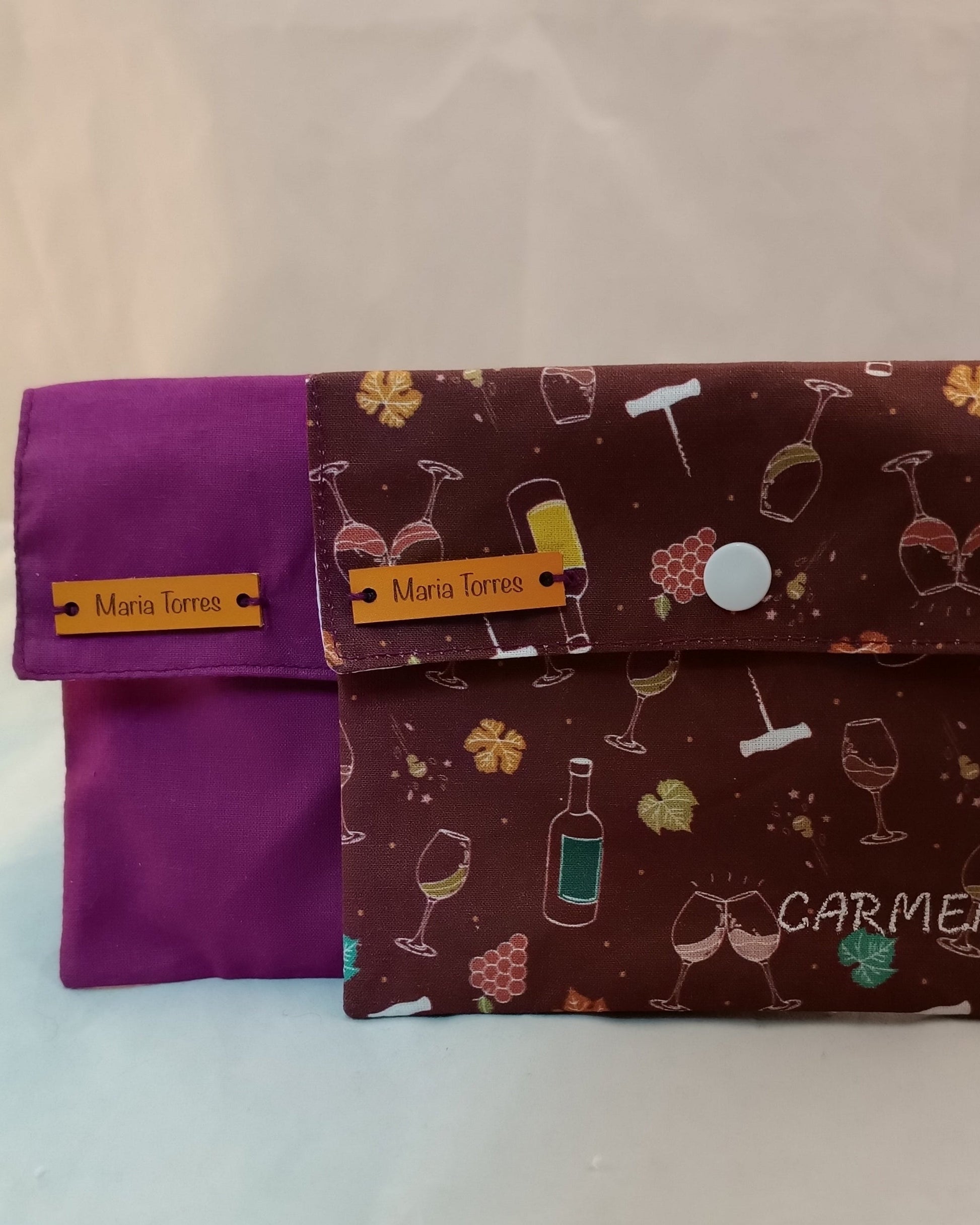 dos neceseres de viaje con solapa y botón blanco con telas morada y estampada con motivos de vino y viña y nombre bordado