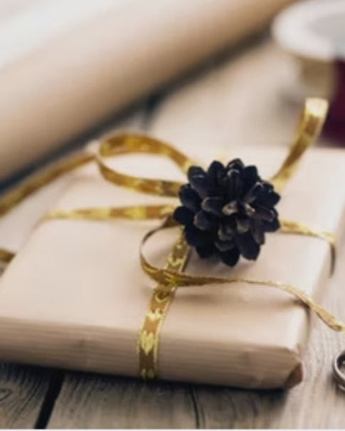 paquete regalo envuelto en papel de craft con lazo dorado y una piña seca sobre él. 