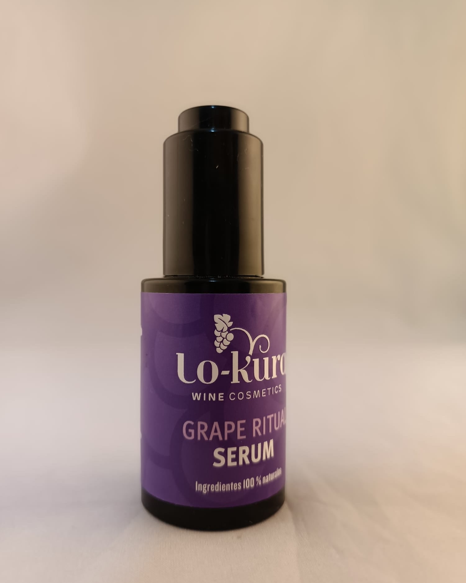 frasco negro de cristal con etiqueta morada en la que se lee grape ritual serum  sobre fondo navideño